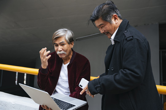 两名高级工程师在城市建筑工地用笔记本电脑在户外工作。