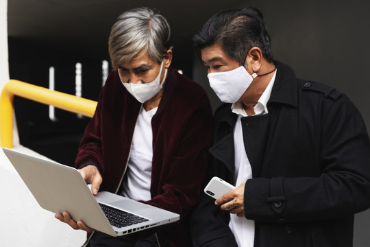 乔维德-19流感大流行期间，两名戴着口罩的高级工程师手持笔记本电脑在户外工作的肖像。