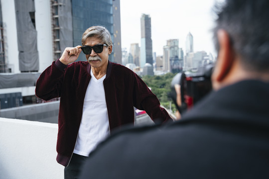 时尚写真——穿着夹克、戴着墨镜的高级男士在城市里与摄影师合影。