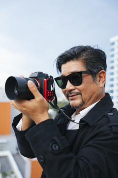 时尚写真——戴墨镜手持无镜相机的老年高级摄影师。