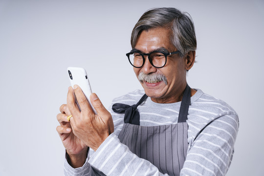 在白色背景上使用智能手机隔离的老服务生的肖像。