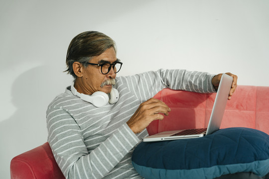 戴眼镜的老人坐在沙发上用笔记本电脑。