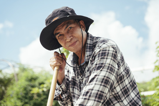 在一个农场里戴着帽子用铲子的亚洲老年农民。