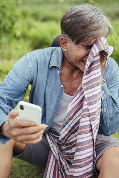 亚洲老年农民在当地农场休息时使用智能手机