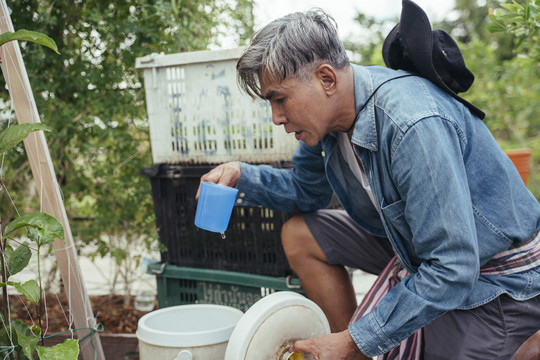 亚洲老年农民从桶里喝水休息。