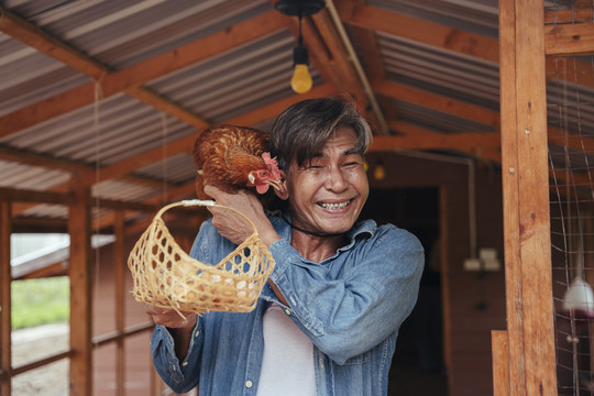 在养鸡场的房子里，亚洲的老年农民手里拿着新鲜的有机蛋篮。