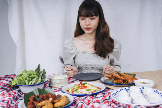 亚洲妇女拿着叉子和勺子在桌子上吃一套伊桑食物的肖像。