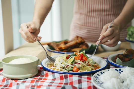 用叉子和勺子吃木瓜沙拉的女人的手。是一种食物概念。