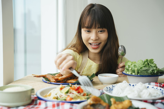 一位年轻的亚洲妇女在家里的餐桌上享受美食。