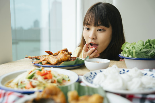 一幅年轻的亚洲妇女看着桌子上的食物，表情惊异的画像。