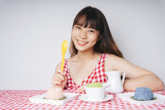 年轻的亚洲女人拿着黄色的勺子，看着粉红色桌子上粘糊糊的饭碗。