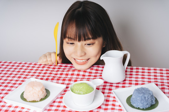 年轻的亚洲女人拿着黄色的勺子，看着粉红色桌子上粘糊糊的饭碗。