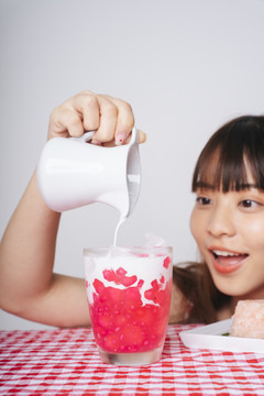年轻的亚洲女人把甜椰奶倒在杯子里的菱角甜点上。