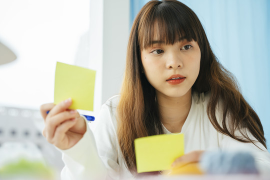 年轻的亚洲黑发女子在便笺纸上写作和计划。