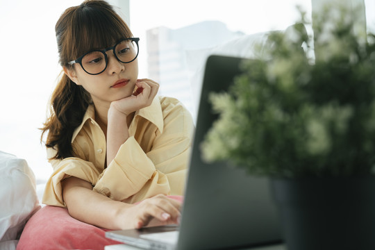 年轻的亚洲黑发女子戴着眼镜在家里用笔记本电脑工作。