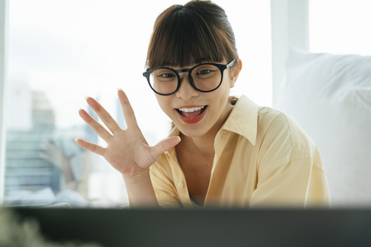 快乐快乐的年轻亚洲黑发女子戴着眼镜在电脑上做视频通话。
