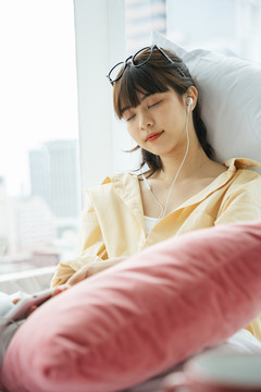 熟睡的亚洲黑发女子在床上用耳机听音乐。