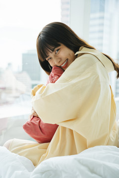 快乐的亚洲年轻黑发女子抱着枕头坐在床上。