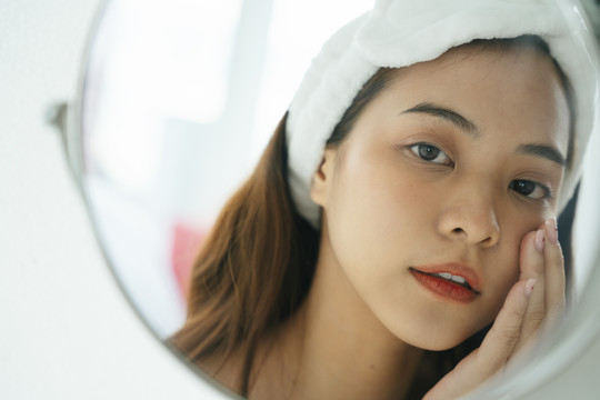 亚洲年轻黑发女性在镜子中进行面部护理的特写照片。