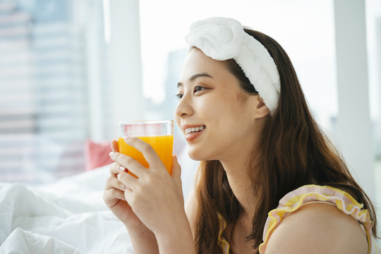 年轻的亚洲黑发女子戴着白色的头巾，手里拿着一杯橙汁。