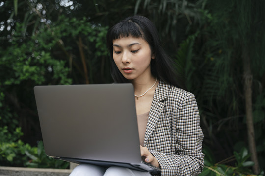穿着正式衬衫的亚洲女商人在户外使用笔记本电脑。