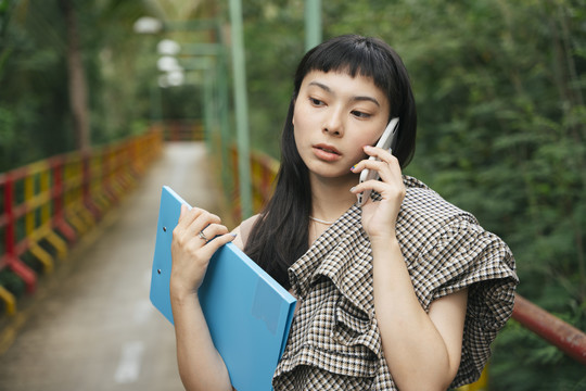 穿着正式衬衫的亚洲女商人拿着文件夹在电话里交谈。