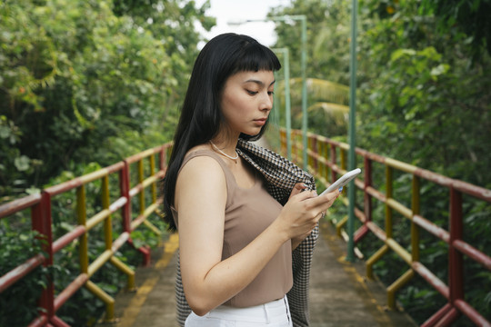 侧视图-穿着正式衬衫的亚洲女商人在户外使用智能手机。