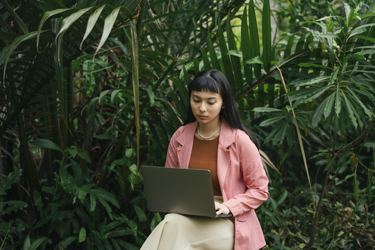 穿着正式衬衫的亚洲女商人坐在椅子上用笔记本电脑。