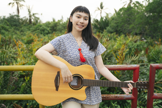 美丽的亚洲年轻女子在户外大自然中弹吉他的画像。