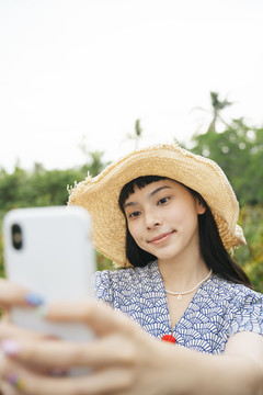 亚洲旅行女性戴草帽用智能手机自拍的时尚写真。