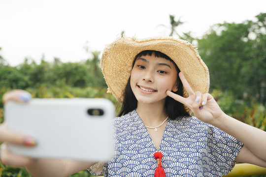 亚洲旅行女性戴草帽用智能手机自拍的时尚写真。