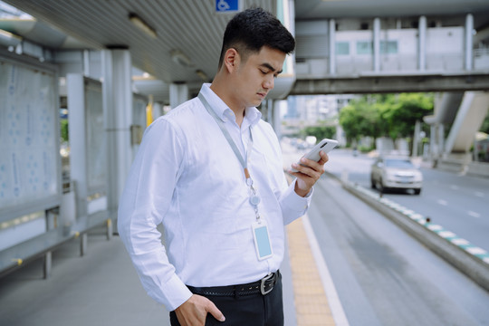 亚洲商人在人行道上用智能手机等公共汽车。