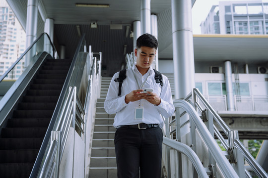亚洲商人在城市里用智能手机走楼梯。