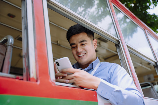 在曼谷，一个快乐的亚洲男人在公共汽车上使用智能手机。