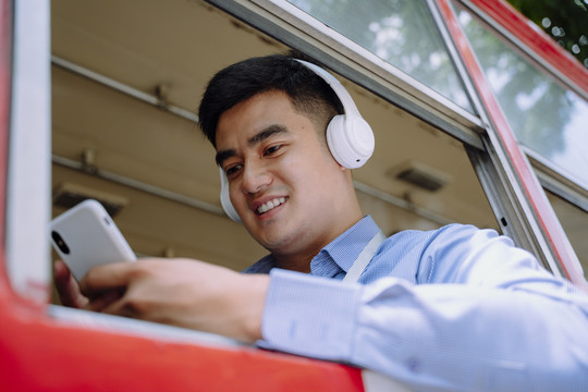在曼谷的一辆公共汽车上，一位兴高采烈的亚洲人用智能手机用无线耳机听音乐。