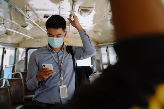 在曼谷的一辆公共汽车上，亚洲商人戴着智能手机面具。