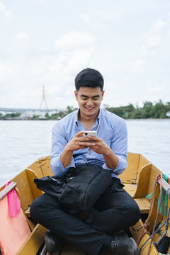 在泰国曼谷，一位亚洲商人正在使用电话和乘船旅行。