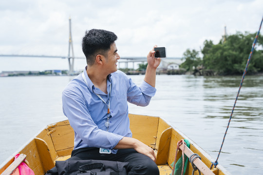 亚洲商人在曼谷用智能手机拍照乘船旅行。