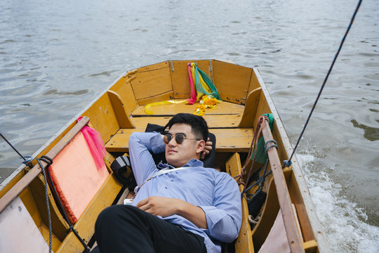 在曼谷，亚洲商人戴着墨镜睡在木船上。
