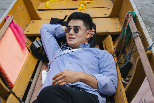 在曼谷，亚洲商人戴着墨镜睡在木船上。
