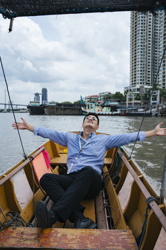 在曼谷，一位亚洲商人坐在船上戴着墨镜。度假旅行。