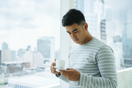 亚洲男人用智能手机拿着一杯咖啡。