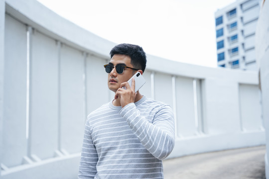 时尚亚洲成年男子戴墨镜打电话的画像。