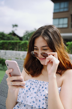 美丽的亚洲女人在酒店的沙滩椅上用智能手机戴眼镜。