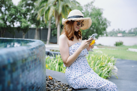 美丽的亚洲女游客在度假酒店泳池边使用智能手机。