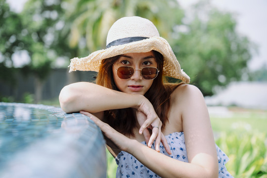 特写肖像-美丽的亚洲女游客，戴着太阳镜和帽子在泳池边。