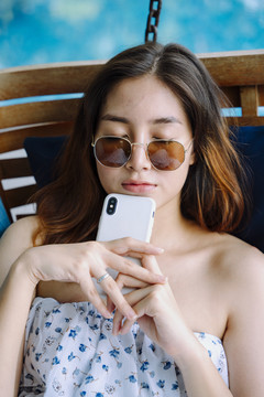 特写写真-美丽的亚洲女旅行者戴墨镜拿着智能手机睡在沙发上。