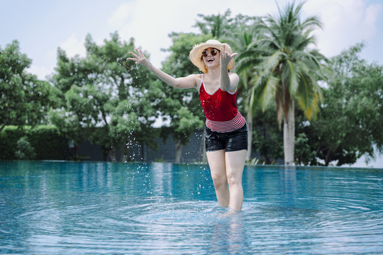 美丽的亚洲女游客在室外游泳池里泼水。