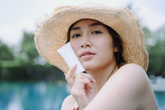 特写镜头——美丽的亚洲女游客在游泳池戴着涂有防晒霜的帽子。