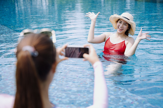 美丽的亚洲女游客喜欢用智能手机在游泳池拍照。
